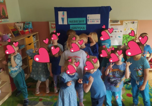 Dzieci ubrane na niebiesko pozują na tle dekoracji Niebieskich Igrzysk.