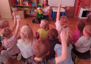 Dzieci siedzą przed kobietą trzymającą maskotkę smoka.